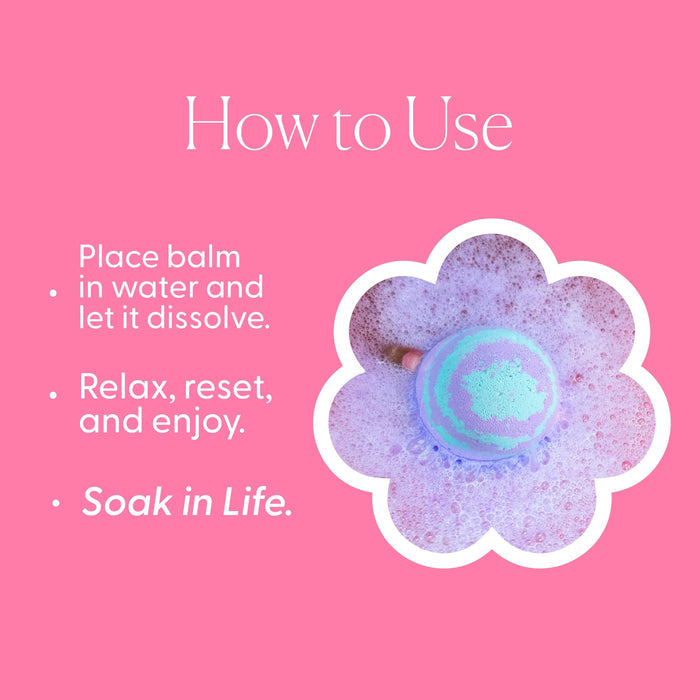 A lavender-colored bath bomb rests beside its cylindrical container labeled “MUSEE - DREAMWEAVER THERAPY BATH BALM,” offering a soothing bath experience infused with calming chamomile and lavender oil.