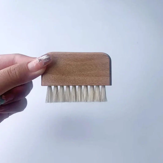 Small wooden brush with bristles held by a hand against a light blue background