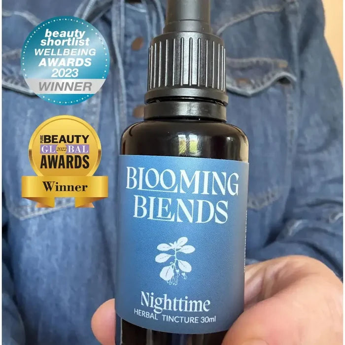 Bottle of 'Blooming Blends' Nighttime Herbal Tincture held by a person, with awards displayed.