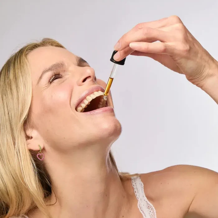 Woman taking a dropper of liquid into her mouth against a plain background