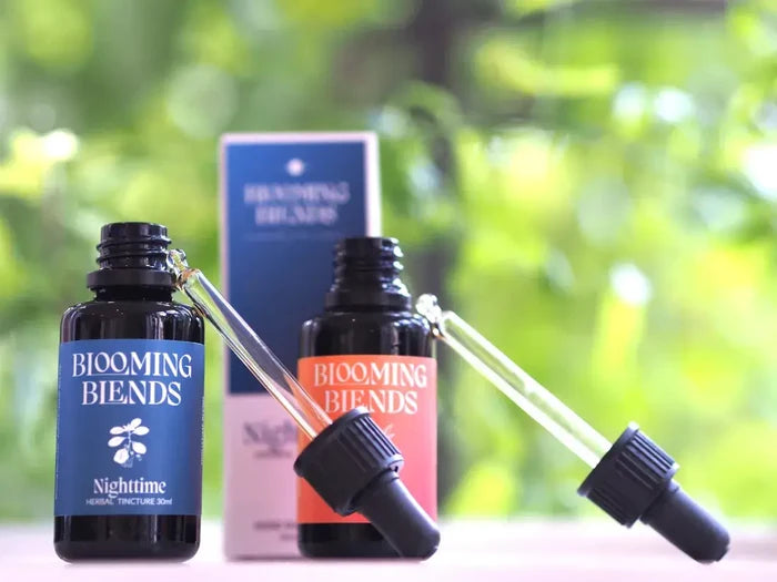 Two bottles of Blooming Blends with droppers on a blurred green background