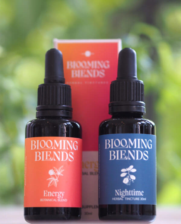 Two bottles of Blooming Blends, one labeled 'Energy' and the other 'Nighttime', with a blurred green background.