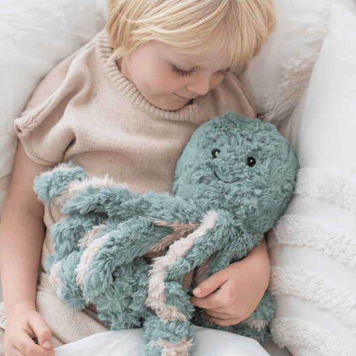 Child holding a soft teal octopus Weighted Teddy on a white blanket