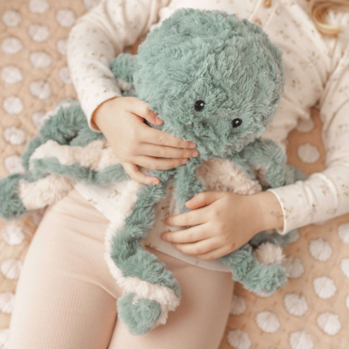 Child holding a green plush octopus Weighted Teddy on a polka dot blanket