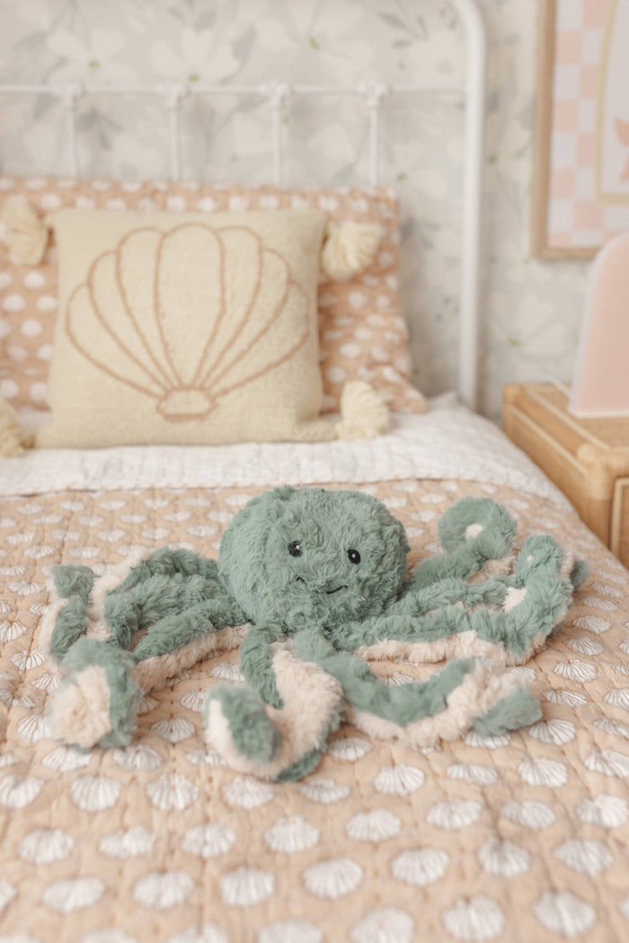Green plush octopus Weighted Teddy on a bed with shell-patterned pillows.