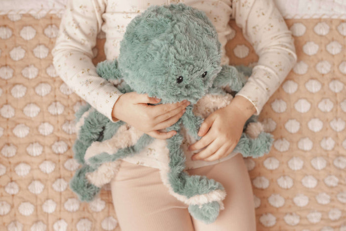Person holding a green plush octopus Weighted Teddy on a polka dot blanket