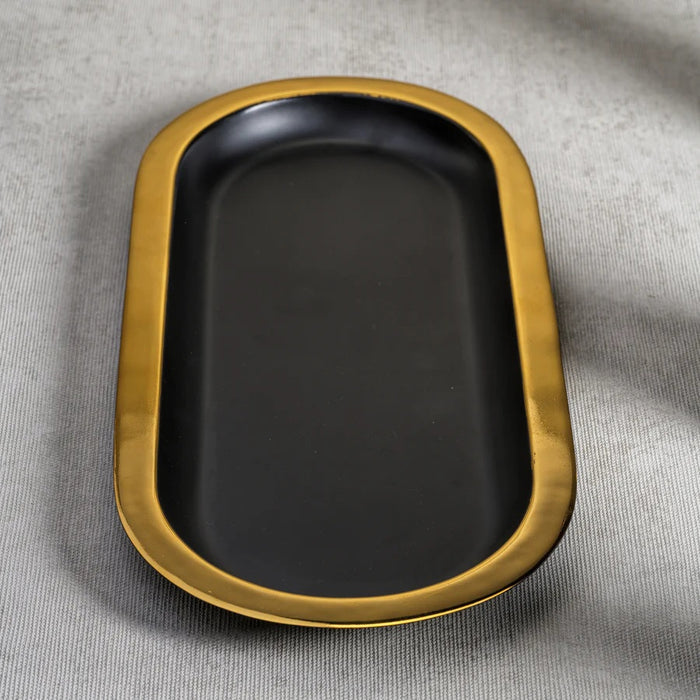 The ZODAX OVAL TRAY - BLACK WITH GOLD BORDER is a modern serving tray with a matte black oval base and a bold gold rim, shown elegantly on a white background.