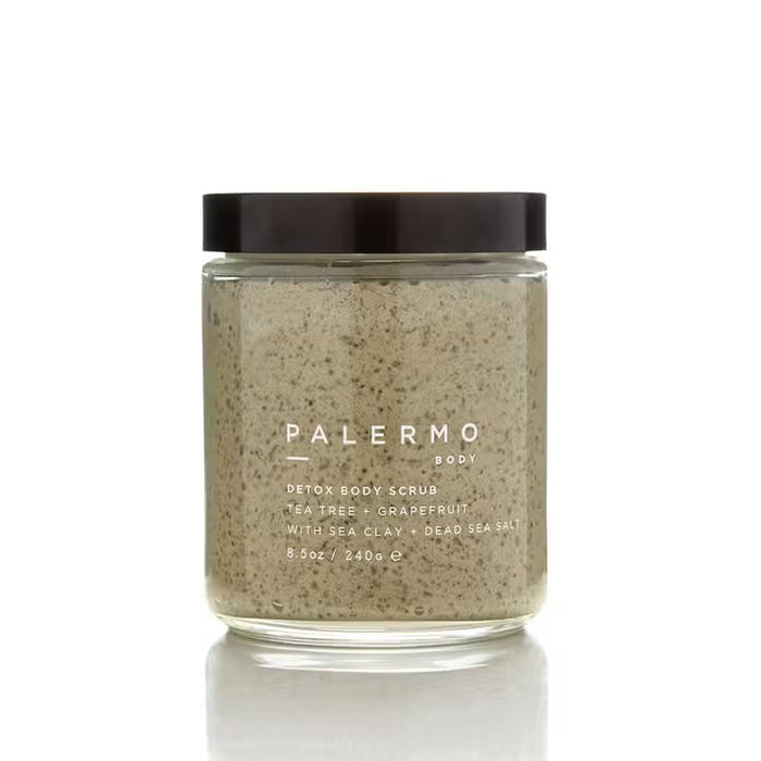 A clear glass jar with a black lid holds PALERMO BODY’s TEA TREE AND GRAPEFRUIT BODY SCRUB, featuring sea clay and Dead Sea salt. The label lists 8.5 oz (240g) of detoxifying exfoliant inside.