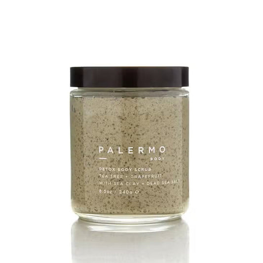 A clear glass jar with a black lid holds PALERMO BODY’s TEA TREE AND GRAPEFRUIT BODY SCRUB, featuring sea clay and Dead Sea salt. The label lists 8.5 oz (240g) of detoxifying exfoliant inside.