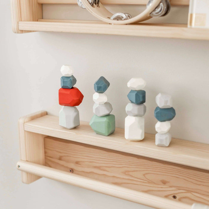 Colorful geometric stone stacks on a wooden shelf against a light wall.