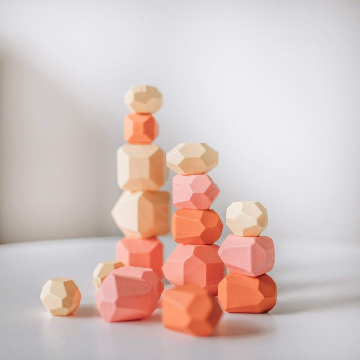 Stack of geometric wooden blocks in various shades of pink and orange on a light background
