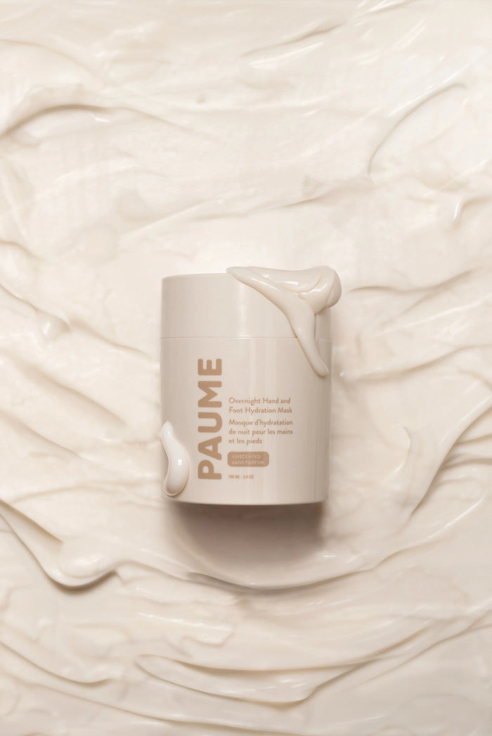 A person with dark skin and manicured nails scoops PAUME - OVERNIGHT HAND AND FOOT HYDRATION MASK. With Panthenol, Shea Butter, and Squalane, this PAUME mask delivers deep hydration to repair dry, cracked skin overnight.
