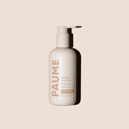 A beige pump bottle labeled "PAUME - PROBIOTIC HAND BALM 10OZ" by PAUME, featuring plant-based emollients, stands upright on a light beige background with a right-cast shadow. The label shows English and French text and a net weight of 10oz.