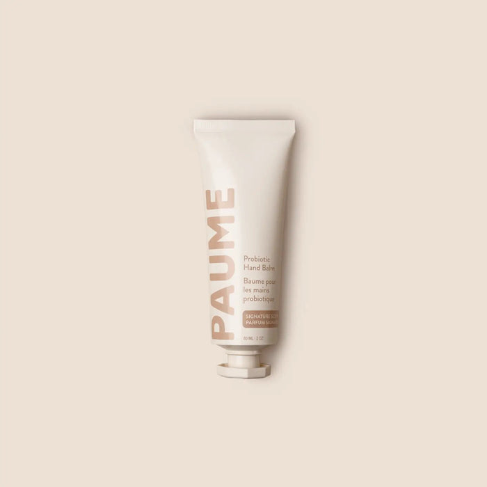 A person applies PAUME - PROBIOTIC HAND BALM 2OZ by PAUME to the back of their hand. Text highlights grapeseed oil, plant-based emollients, and probiotics for hydrating, smoothing, and protecting the skin.