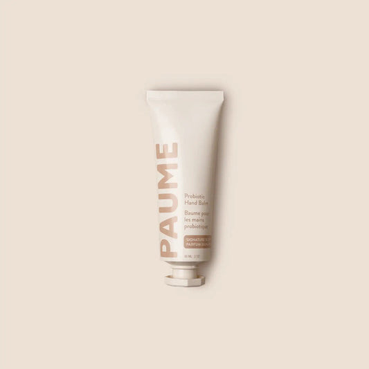 A person applies PAUME - PROBIOTIC HAND BALM 2OZ by PAUME to the back of their hand. Text highlights grapeseed oil, plant-based emollients, and probiotics for hydrating, smoothing, and protecting the skin.