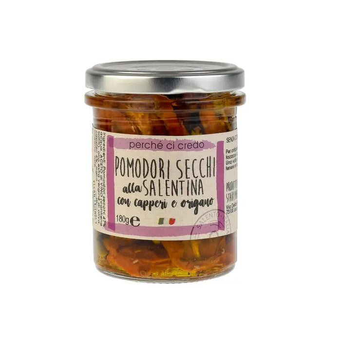 A glass jar of PERCHE CI CREDO - SUN-DRIED TOMATOES by ZIA PIA IMPORTS, with a metal lid and white Italian label. Sun-dried tomatoes with capers and oregano in extra virgin olive oil are visible through the jar.