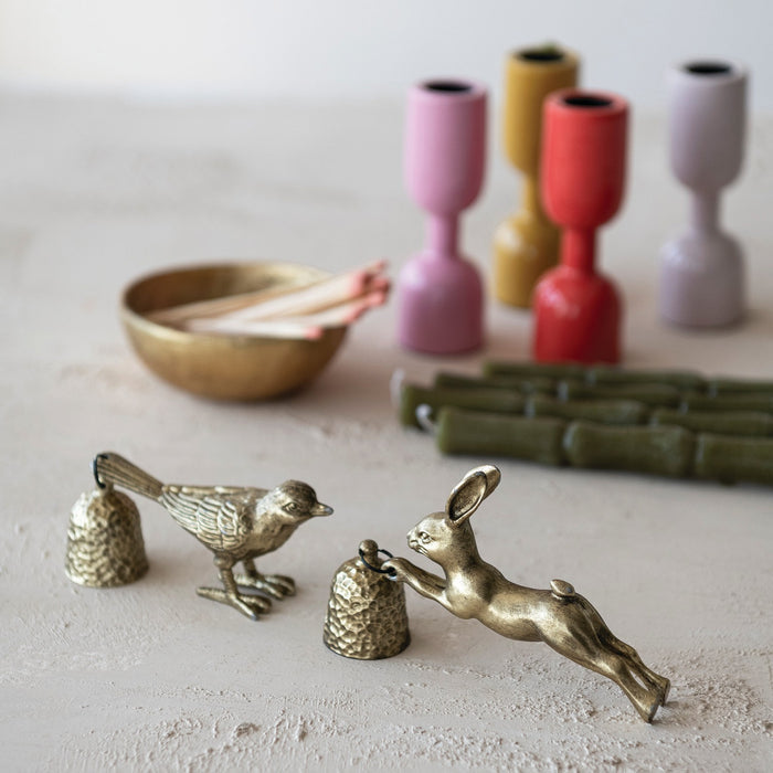 The CREATIVE COOP PEWTER BIRD-SHAPED CANDLE SNUFFER in antique gold finish features a textured, shiny design with a hammered metal bell attached to its tail, standing on two legs for an eye-catching display.