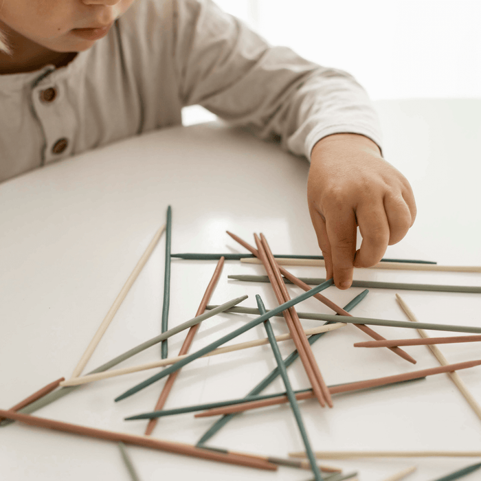 Child carefully playing with colorful sticks in a game of Pick Up Sticks, promoting mindfulness and fine motor skills.