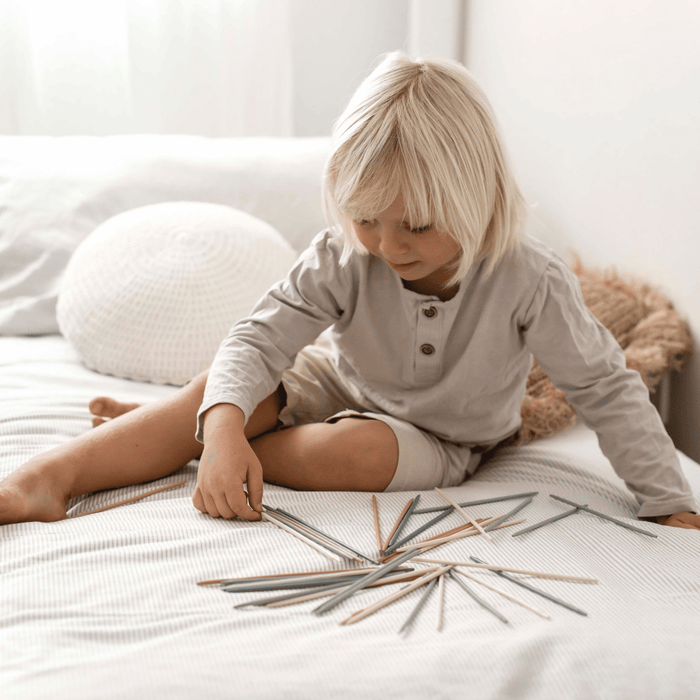 Child playing with Pick Up Sticks, focusing intently on colorful sticks spread out on a bed.