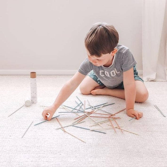 Child playing Pick Up Sticks on the floor, fostering concentration and family fun with colorful wooden sticks.