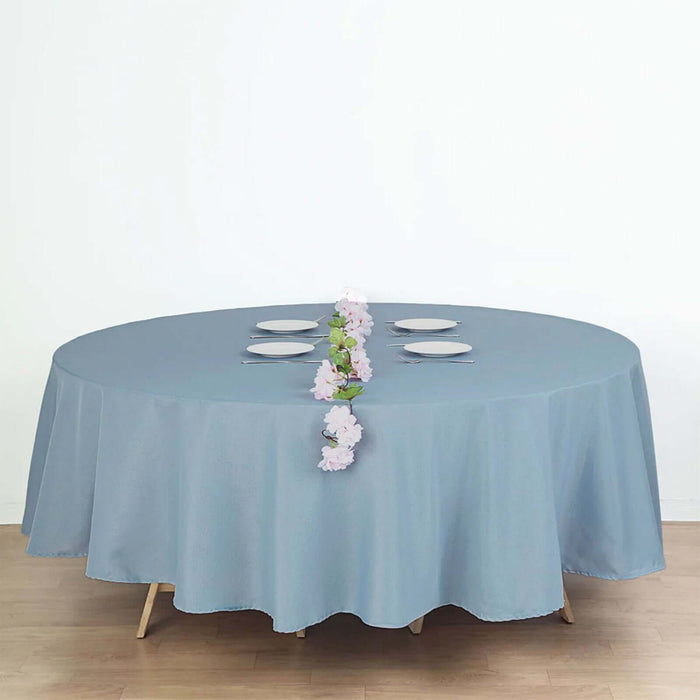 Round blue tablecloth draped over a dining table with plates and a floral centerpiece.