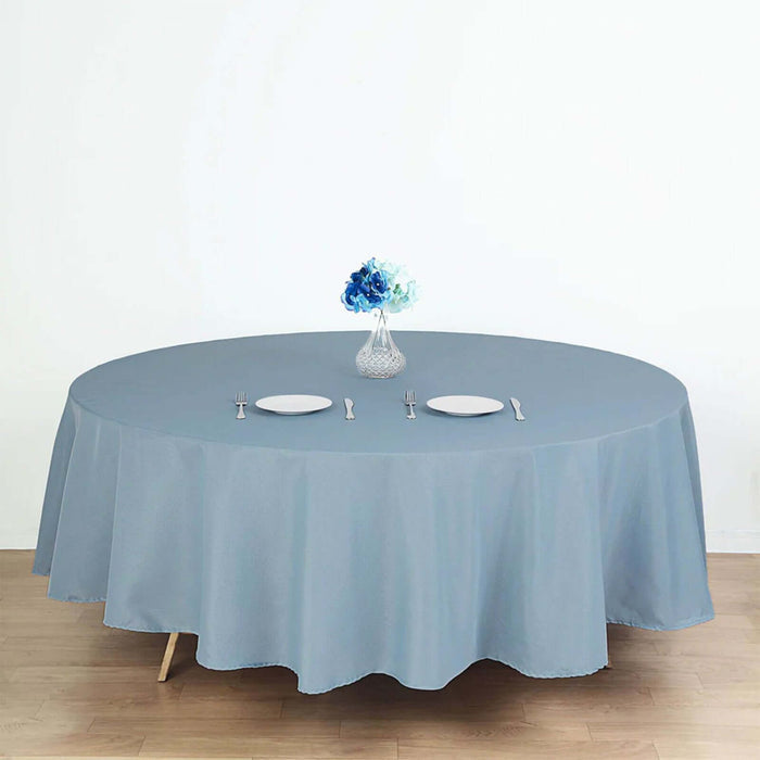 Round blue tablecloth on a wooden table set with plates and a vase of flowers.