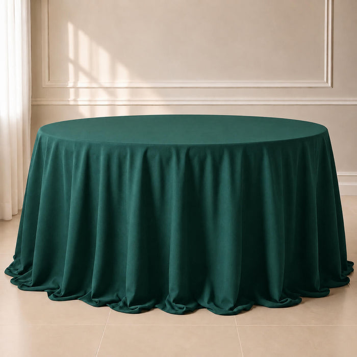 132" round table covered with a dark green tablecloth, set in an indoor room with beige walls, molding, and tiled floor.