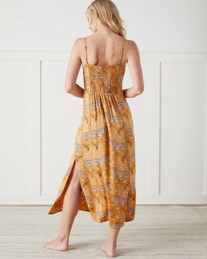 A woman stands barefoot indoors, wearing the PRINTFRESH Bagheera Eco Satin Chic to Sleep Nightie in Tobacco—a long, cheetah-patterned nightgown that captures the effortless elegance of sustainable sleepwear. She is looking down and touching her hair with one hand.