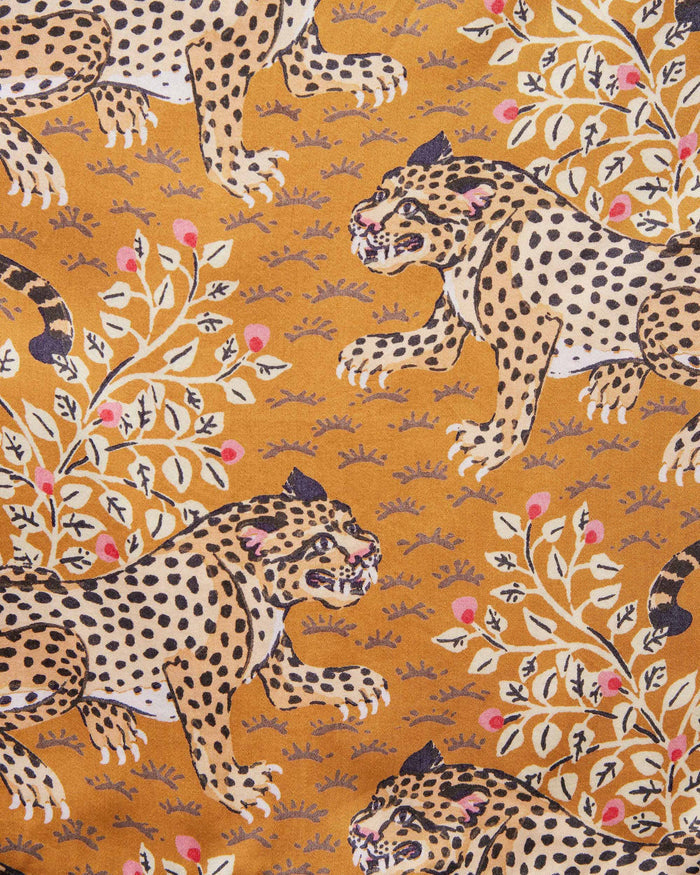 A woman stands barefoot indoors, wearing the PRINTFRESH Bagheera Eco Satin Chic to Sleep Nightie in Tobacco—a long, cheetah-patterned nightgown that captures the effortless elegance of sustainable sleepwear. She is looking down and touching her hair with one hand.