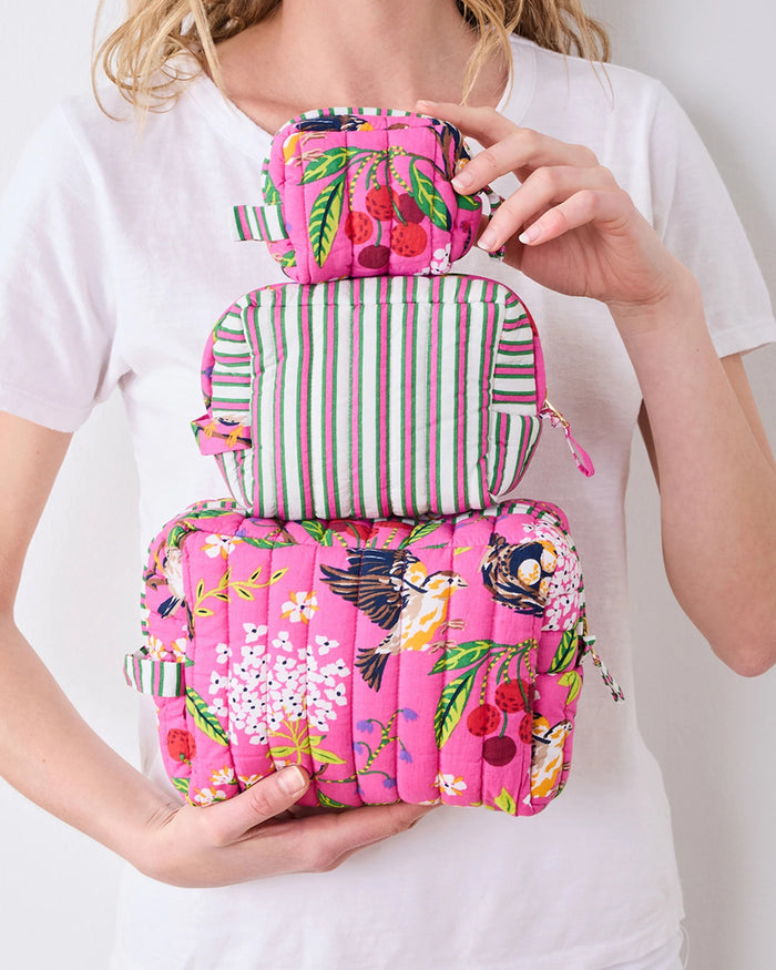 A person in a white shirt holds the PRINTFRESH - BIRD & BLOSSOM THREE POUCH SET by PRINTFRESH, featuring three quilted makeup pouches with colorful floral and striped patterns, nested from smallest to largest.