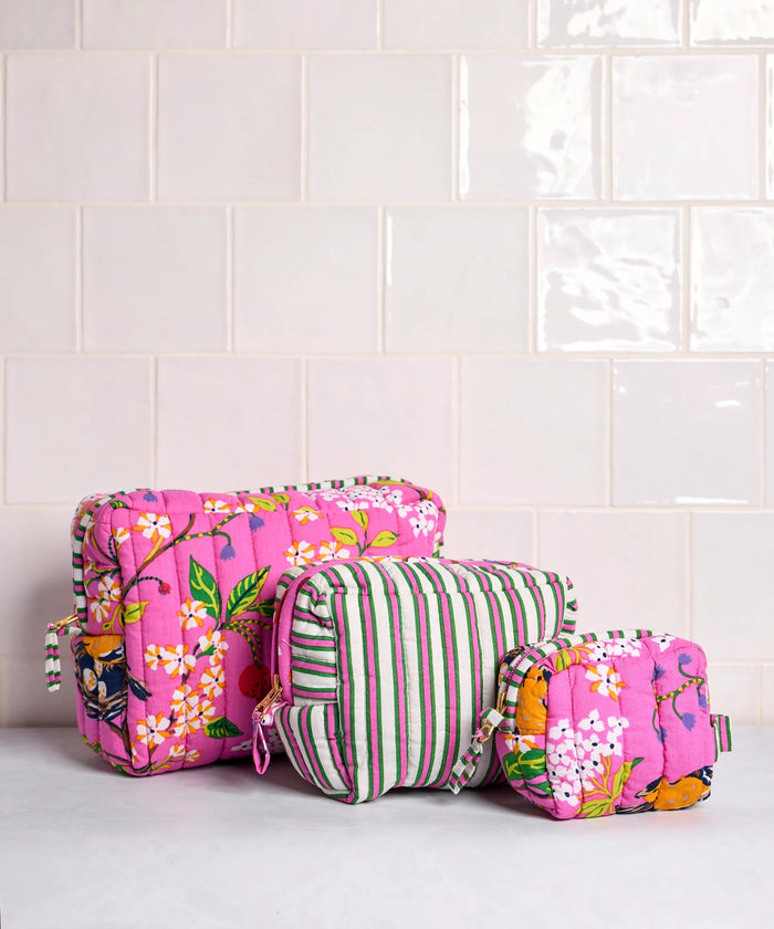 A person in a white shirt holds the PRINTFRESH - BIRD & BLOSSOM THREE POUCH SET by PRINTFRESH, featuring three quilted makeup pouches with colorful floral and striped patterns, nested from smallest to largest.