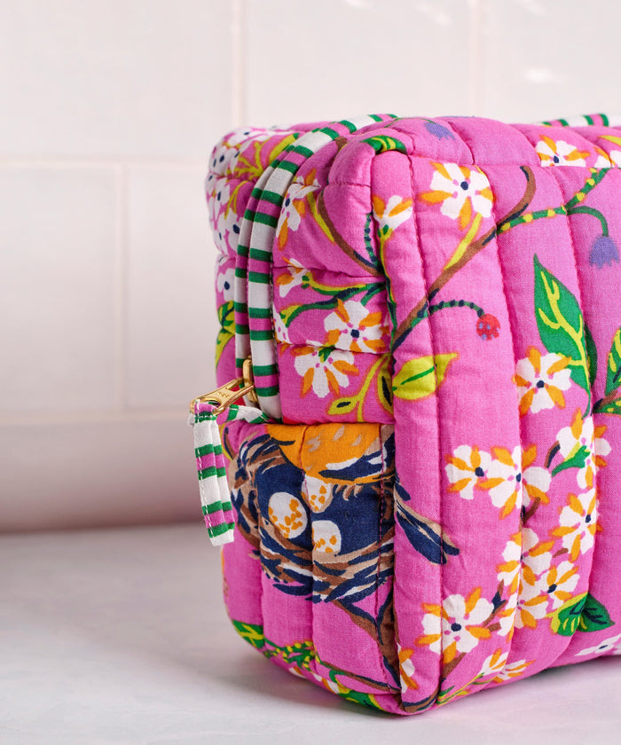 A person in a white shirt holds the PRINTFRESH - BIRD & BLOSSOM THREE POUCH SET by PRINTFRESH, featuring three quilted makeup pouches with colorful floral and striped patterns, nested from smallest to largest.