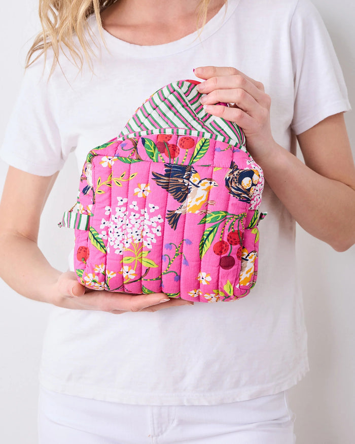 A person in a white shirt holds the PRINTFRESH - BIRD & BLOSSOM THREE POUCH SET by PRINTFRESH, featuring three quilted makeup pouches with colorful floral and striped patterns, nested from smallest to largest.