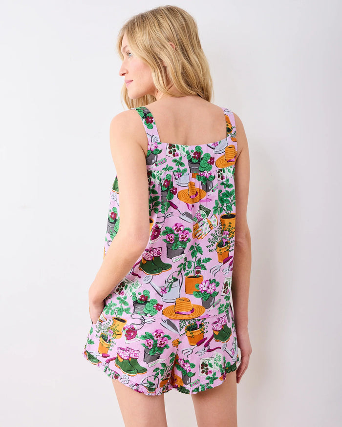 A woman with long blonde hair stands against a plain white wall, looking slightly to the side and smiling softly, wearing the PRINTFRESH - GREEN THUMB BACK TO BED PAJAMA SHORT SET by PRINTFRESH—a colorful floral sleepwear set inspired by vintage styles.