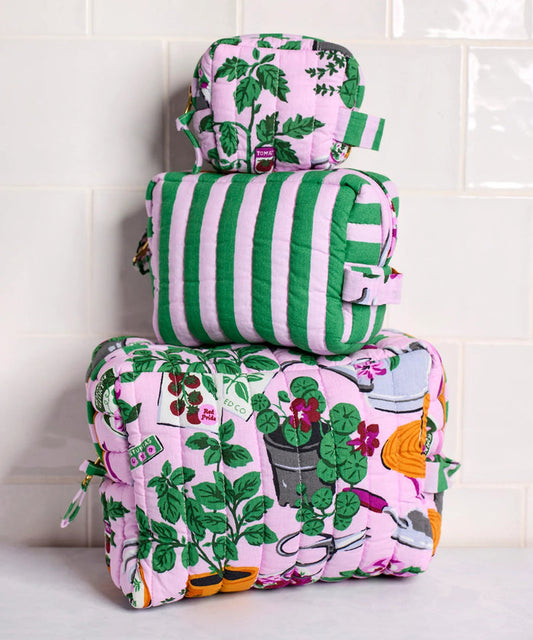 A person in a white shirt holds the PRINTFRESH - GREEN THUMB THREE POUCH SET by PRINTFRESH, featuring three quilted travel pouches with floral and striped patterns, stacked from largest to smallest, against a plain background.