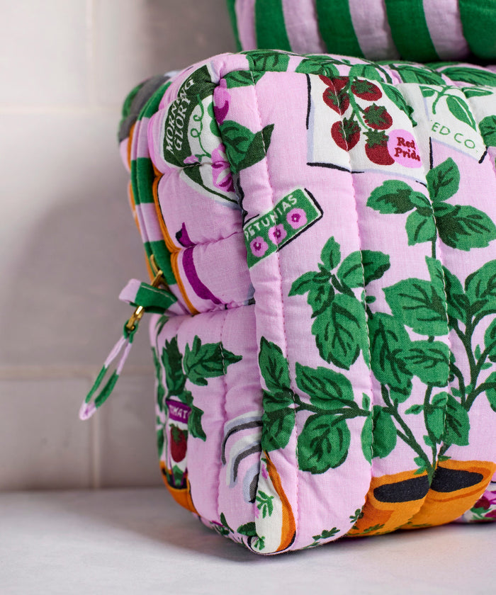 A person in a white shirt holds the PRINTFRESH - GREEN THUMB THREE POUCH SET by PRINTFRESH, featuring three quilted travel pouches with floral and striped patterns, stacked from largest to smallest, against a plain background.
