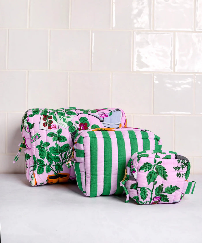 A person in a white shirt holds the PRINTFRESH - GREEN THUMB THREE POUCH SET by PRINTFRESH, featuring three quilted travel pouches with floral and striped patterns, stacked from largest to smallest, against a plain background.