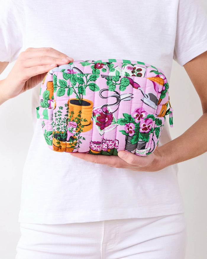 A person in a white shirt holds the PRINTFRESH - GREEN THUMB THREE POUCH SET by PRINTFRESH, featuring three quilted travel pouches with floral and striped patterns, stacked from largest to smallest, against a plain background.