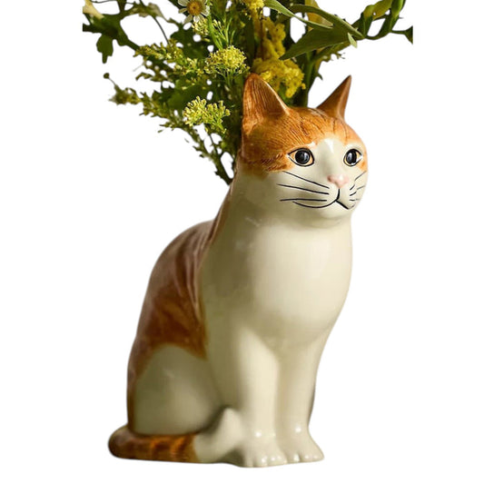 The QUAIL CERAMICS - SQUASH CAT FLOWER VASE by QUAIL DESIGNS is a hand-painted stoneware vase shaped like a sitting orange cat, with green foliage and yellow flowers appearing to grow from its back.