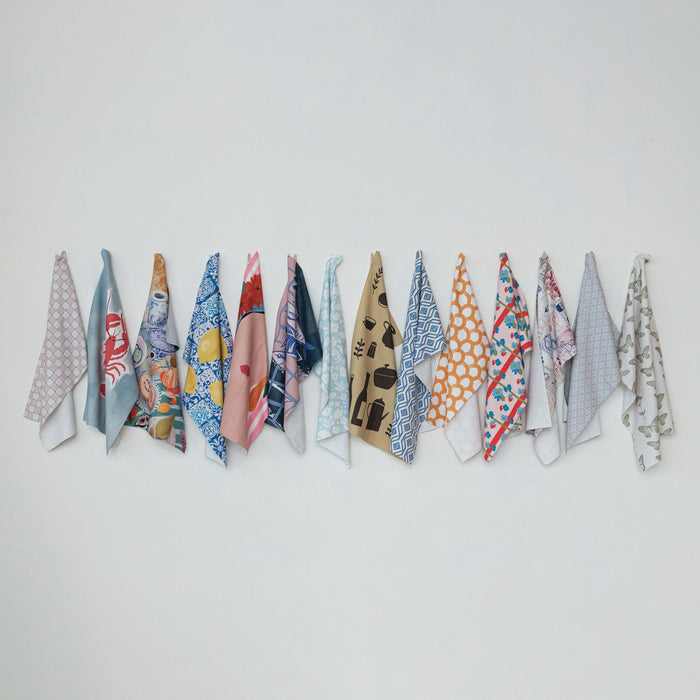 Thirteen CREATIVE COOP RECYCLED MICROFIBER TEA TOWELS, each featuring a unique design—lemons, seafood, butterflies, abstract motifs, dishes, and a woman with a floral headdress—are arranged in three rows on a white background.