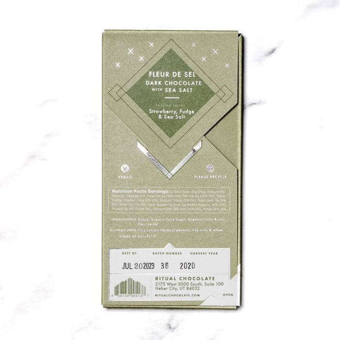 A green RITUAL CHOCOLATE - FLEUR DE SEL CHOCOLATE BAR 70% CACAO with silver geometric designs and text on the wrapper, shown on a white marble background.
