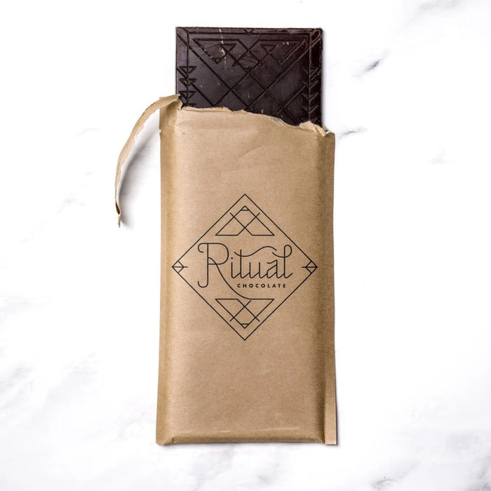 A green RITUAL CHOCOLATE - FLEUR DE SEL CHOCOLATE BAR 70% CACAO with silver geometric designs and text on the wrapper, shown on a white marble background.