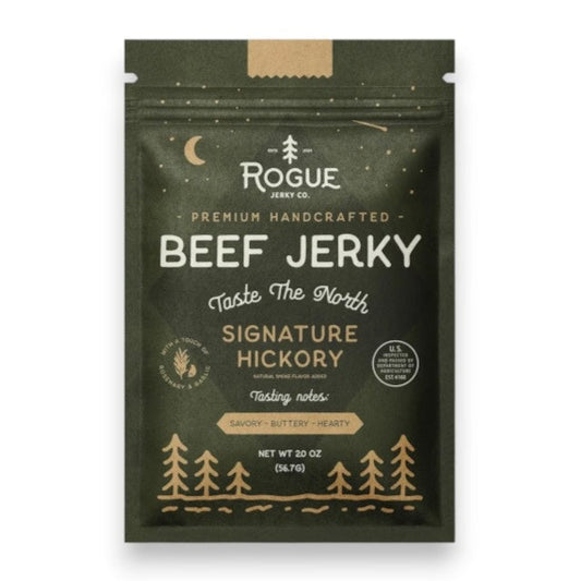 A dark green pouch of ROGUE JERKY - HICKORY BEEF JERKY by ROGUE JERKY CO., featuring forest and moon imagery, labeled “Premium Handcrafted” and “Taste The North.” This savory, buttery, hearty sugar free jerky is an ideal keto friendly snack. Net weight: 2 oz.