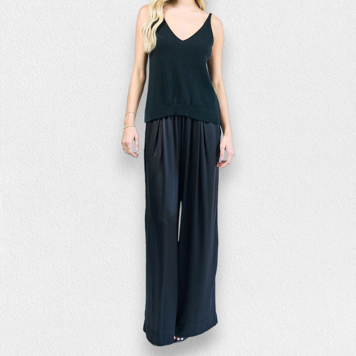 A woman stands against a light textured background wearing ROSE & CROWN’s SATIN TROUSER, paired with a sleeveless V-neck black top. Her effortlessly chic look is perfect for an evening out.