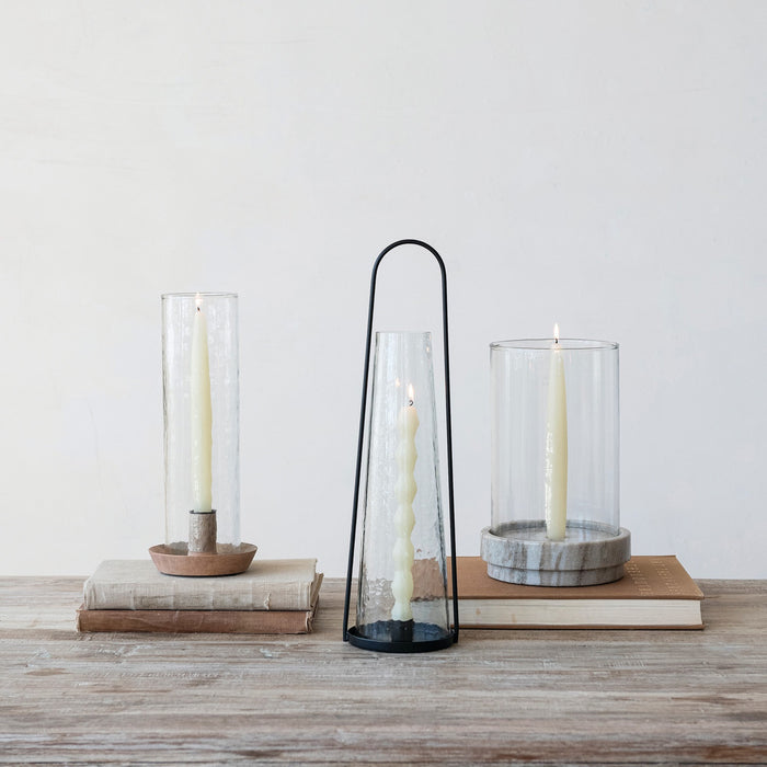 The ROUND METAL LANTERN TAPER HOLDER WITH HAMMERED GLASS HURRICANE by CREATIVE COOP features a tall, black metal frame and a cone-shaped hammered glass hurricane for a modern, minimalist look with sleek lines and transparent materials.