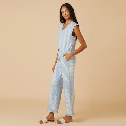 A woman with long dark hair wears the SOFTIES Dream Ruffle V-Neck with Cropped Pant in Sky Blue Stripe as she looks off to the side against a beige background.