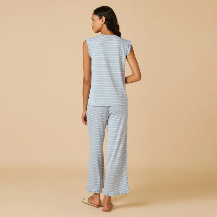 A woman with long dark hair wears the SOFTIES Dream Ruffle V-Neck with Cropped Pant in Sky Blue Stripe as she looks off to the side against a beige background.