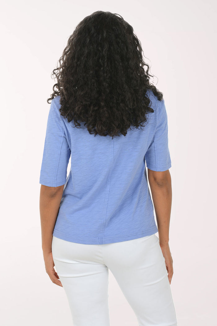 Person wearing a blue top and white pants on a light pink background