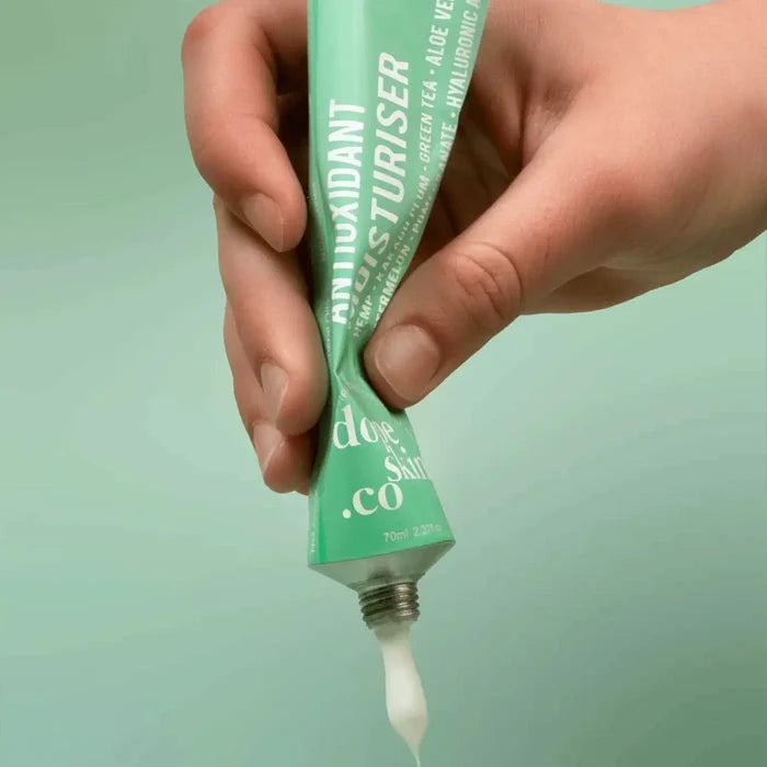 Hand holding a green tube of skincare product with a light green background