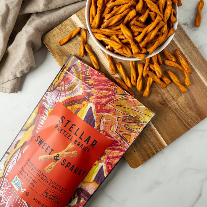 A vibrant bag of STELLAR SNACKS - SWEET & SPARKY PRETZEL BRAIDS, showcasing bold red and orange abstract artwork, flavorful buffalo-inspired seasoning, and clear product information on the front—the ideal pick for those who love spicy snacks.